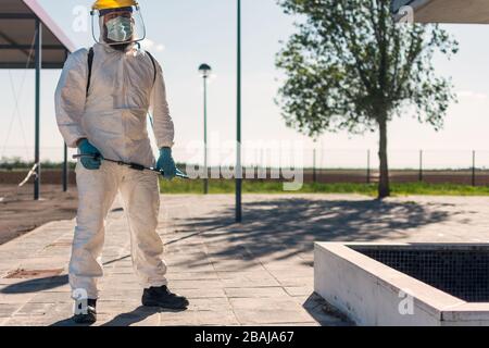 Mann, der einen persönlichen Schutzanzug (psa), Handschuhe, Maske und Gesichtsschutz von NBC trägt und die Straßen mit einem Rucksack mit unter Druck stehendem Spray säubert Stockfoto