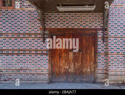 Grunge aus Holz dekorierte gewölbte Eingangstore mit Holzdach oben an der Wand mit schwarzen und roten Ziegelsteinen mit weißer Naht Stockfoto