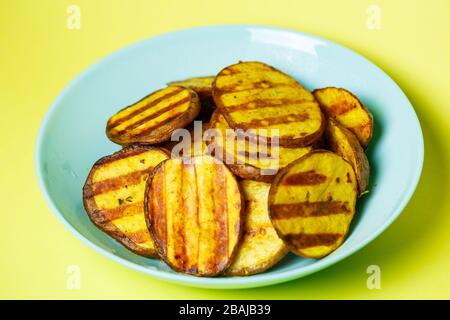 Gegrillte Kartoffeln goldbraun in einem blauen Teller auf gelbem Grund Stockfoto