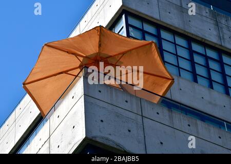 Geringer Blick auf einen Eckteil eines minimalistisch grauen Betongebäudes mit einem leuchtend orangefarbenen Sonnenschirmstab Stockfoto