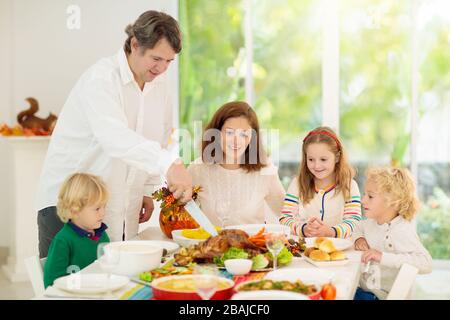 Familie mit Kindern, die Thanksgiving Abendessen essen. Geröstete truthahn- und Kürbiskuchen auf Esstisch mit Herbstdekoration. Eltern und Kinder mit Festiv Stockfoto