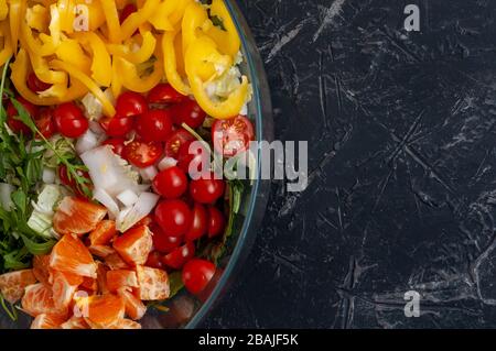 Frischer Salat mit süßen Paprika, Kirschtomaten, Chinakohl, Mandarinen, Rubel und Olivenöl in einer Glasschale auf dunklem Hintergrund Stockfoto