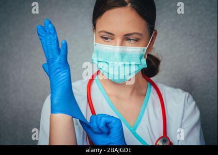 Schutz vor ansteckenden Erkrankungen, Coronavirus. Schöne weibliche Ärztin oder Krankenschwester, die Schutzmaske und Latex- oder Gummihandschuhe auf grauem Rücken trägt Stockfoto
