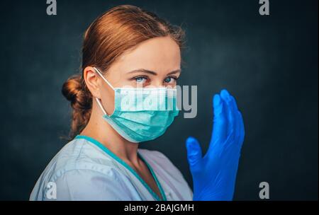 Schutz vor Coronavirus. Junge Frau Doktor in weißer Uniform mit Maske und Handschuhen. Schwarzer Hintergrund Stockfoto