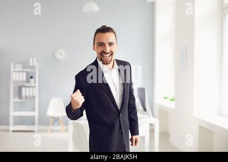 Der Geschäftsmann in einer schwarzen Jacke fuhr lächelnd über die Arme, während er im Büro stand Stockfoto