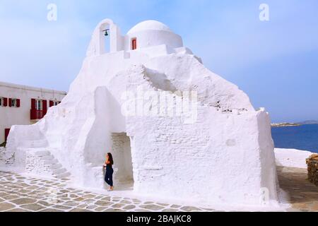 Mykonos, Griechenland - 23. April 2019: Frau posiert für Foto in der Nähe der weißen Paraportiani-Kirche auf der Insel Myconos Stockfoto