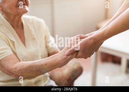 Krankenschwester tröstet ihre ältere Patientin, indem sie ihre Hände hält Stockfoto