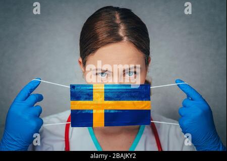 Coronavirus in Schweden Frauenarzt Porträt halten Gesicht schützen chirurgische Maske mit Schweden Nationalflaggen. Krankheit, Virus Covid-19 in Schweden, Con Stockfoto