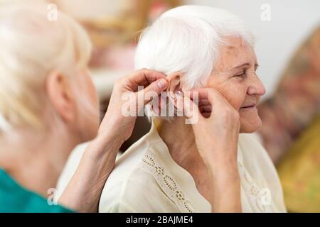 Weibliche Ärztin, die Hörgeräte am Ohr der älteren Frau anwendet Stockfoto