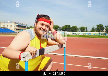 Fetter lustiger Mann, der sich auf der Strecke im Stadion aufsitzt Stockfoto