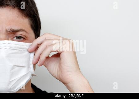 Junger Mann, der Gesichtsmaske trägt, um sich vor Coronavirus zu schützen. Innenfoto auf weißem Hintergrund. Nahaufnahme mit halber Teilfläche. Stockfoto