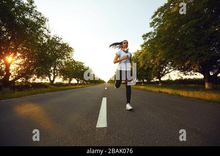 Mädchen Läuferin läuft im Morgengrauen auf der Straße die Sonne Stockfoto