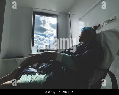 Auf dem medizinischen Stuhl liegend, befindet sich das Senioren-Männchen im modernen Krankenhaus in Frankreich, das nach einer Infektion mit dem Virus Coronavirus ruht - großes Fenster der Hoffnung mit Sonnenfleckchen Stockfoto
