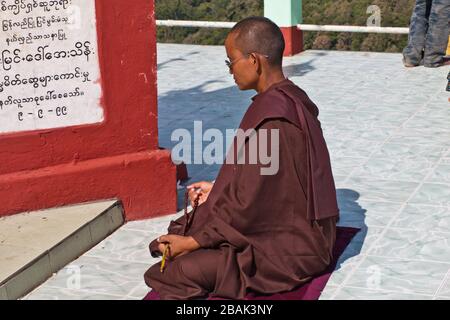 Eine buddhistische Nonne meditiert vor einer Steinplatte mit Theravada-Text, Taung Kalat, Myanmar Stockfoto