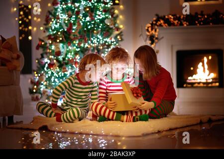 Kinder am Weihnachtsbaum und Kamin auf Heiligabend. Familie mit Kindern Weihnachten zu Hause feiern. Junge und Mädchen in passenden Schlafanzug Dekoration Weihnachten Stockfoto