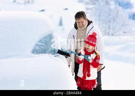 Vater und Kind Bürsten und Schneeschaufeln off-Auto nach Sturm. Eltern und Kind mit Winter Bürste und Schaber clearing Familie Auto nach Übernachtung sno Stockfoto