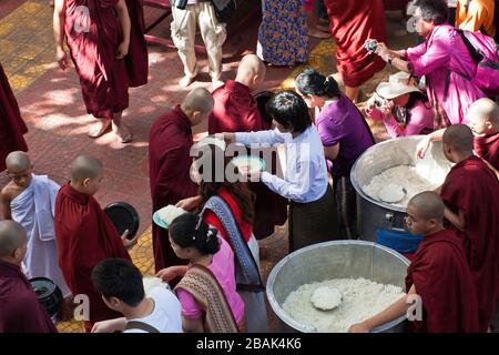 Touristen, die während des weltweit größten Mittagessen buddhistischer Mönch im Mahagandayon-Kloster Mandalay in Myanmar Essen verteilen Stockfoto