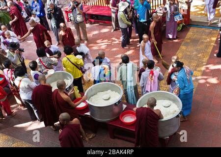 Touristen, die während des weltweit größten Mittagessen buddhistischer Mönch im Mahagandayon-Kloster Mandalay in Myanmar Essen verteilen Stockfoto