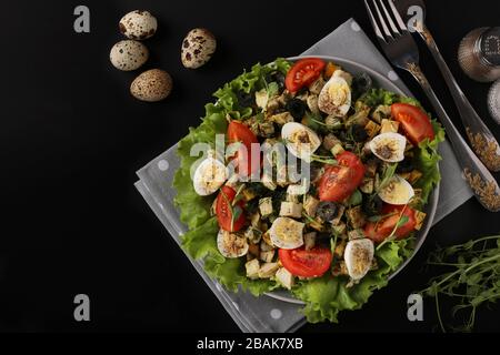 Biosalat mit Huhn, Kirschtomaten, Wachteleiern, schwarzen Oliven und Mikrogrüns vor dunklem Hintergrund, gesunder Esstag Stockfoto