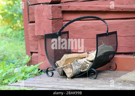 Brennholz Halter aus Metallnetz. Es gibt etwas Brennholz im Halter, der sich auf einer hölzernen Veranda eines Retro-Stil Sommerhauses in Finnland befindet. Stockfoto