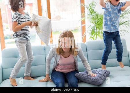 Mutter mit Kopfschmerzen und Kinder springen auf dem Sofa Stockfoto