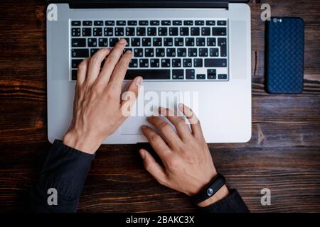 Ein männlicher Programmierer in einem schwarzen Hemd arbeitet an einem Laptop, Nahaufnahme des Programmcodes und die Hände des Entwicklers auf einem Laptop. Moderner junger Programmierer sitzt Stockfoto