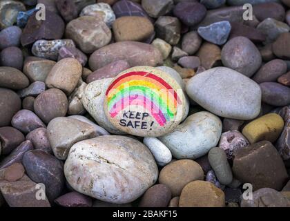 Kiesel mit Regenbogen und den Worten „Keep Safe“ Geschrieben darauf in einem Garten in Großbritannien als Eine Botschaft der Hoffnung während der Coronavirus-Pandemie Stockfoto