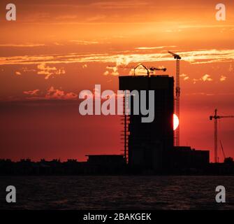 Bau- und Ski-Scraper-Gebäude und Kran gegen bunten Himmel mit Sonne. Baukonzept. Stockfoto