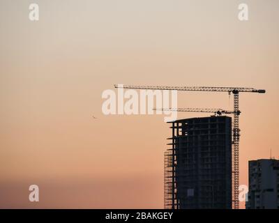 Bau- und Ski-Scraper-Gebäude und Kran gegen bunten Himmel mit Sonne. Baukonzept. Stockfoto
