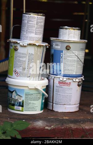 Mehrere halb gebrauchte Farbbehälter mit unterschiedlicher Farbe. Die Eimer sind in zwei Stapel gestapelt. Fotografiert in einem finnischen Sommerhaus im Juli. Stockfoto