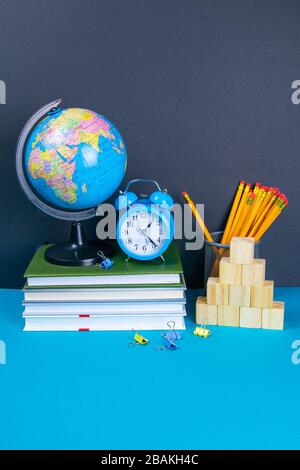 Der Globus und die Uhr stehen auf einem Stapel von Büchern, neben einem Glas Bleistifte und die Pyramide ist mit Holzwürfeln gefaltet Stockfoto