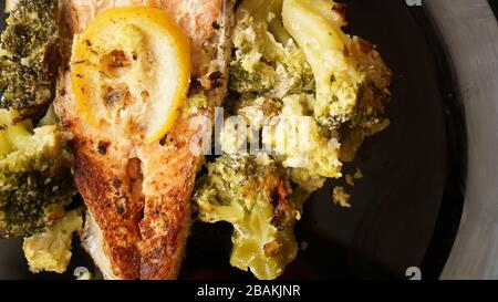 Blick auf gegrilltes Lachssteak auf schwarzem Teller mit Gemüsegarnierung aus Brokkoli Stockfoto