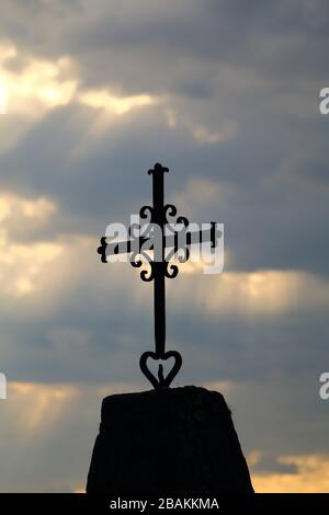 Ein sehr altes schwarzes christenkreuz mit einem wolkigen Himmel im Hintergrund - fotografiert im Hochformat Stockfoto