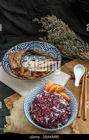 Lachskabutoni gedämpft mit süßer Sojasoße mit goldenem Nadelpilz und in Scheiben geschnittenem ​​ginger serviert mit Riceberry-Reis auf japanischer Schüssel. Traditionell Stockfoto