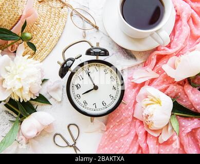Guten Morgen. Tee, Wecker und Blumenstrauß aus weißem Pony auf Marmor-Hintergrund. Flaches Lay. Draufsicht. Kopierbereich. Stockfoto