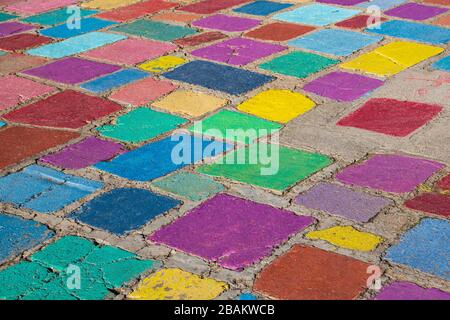 Rustikale Betonfliesen in einem zufälligen Muster, die in lebhaften Farben von lila, grün, blau und rot in einem Außenboden gemalt sind Stockfoto