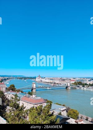 Wunderschönes Panorama von Budapest an einem sonnigen Tag. Brücke, Fluss und kleine Gebäude. Vertikales Foto. Budapest, Ungarn Stockfoto