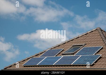 Neu errichtete Häuser in den Niederlanden mit Solarpaneelen, die auf dem Dach gegen einen sonnigen Himmel nahe an neuen schwarzen Solarpaneelen angebracht sind Stockfoto