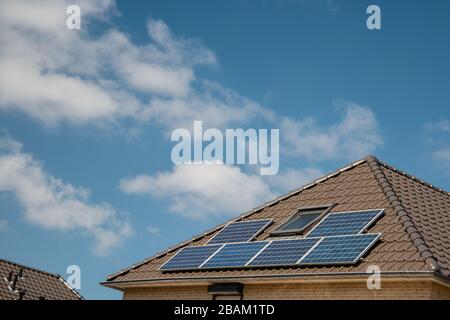 Neu errichtete Häuser in den Niederlanden mit Solarpaneelen, die auf dem Dach gegen einen sonnigen Himmel nahe an neuen schwarzen Solarpaneelen angebracht sind Stockfoto