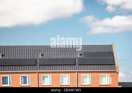 Neu errichtete Häuser in den Niederlanden mit Solarpaneelen, die auf dem Dach gegen einen sonnigen Himmel nahe an neuen schwarzen Solarpaneelen angebracht sind Stockfoto