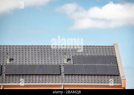 Neu errichtete Häuser in den Niederlanden mit Solarpaneelen, die auf dem Dach gegen einen sonnigen Himmel nahe an neuen schwarzen Solarpaneelen angebracht sind Stockfoto