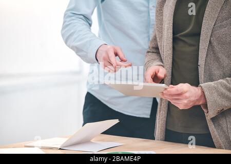 Nahaufnahme nicht erkennbarer Kollegen, die am Tisch stehen und Tablet verwenden, während sie an einem neuen Online-Projekt arbeiten Stockfoto