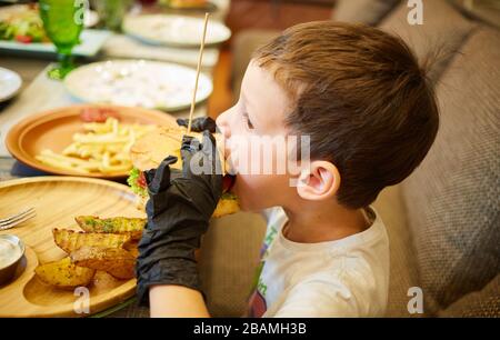 Der stattliche kleine Junge Burger essen in schwarzem Gummi Handschuhe. Stockfoto