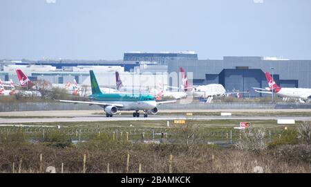 Ein Aer Lingus Airbus A320-214 bewegt sich auf der Startbahn des Flughafens Gatwick, vor einigen der geerdeten Virgin Atlantic Fleet. Stockfoto