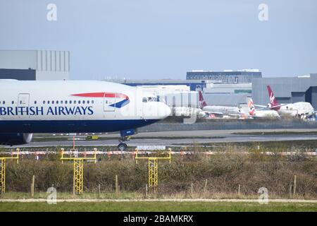 Eine Boeing 777-236 der British Airways fährt zur Startbahn am Flughafen Gatwick und fährt vor einigen geerdeten Flugzeugen der Virgin. Stockfoto
