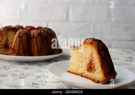 Kuchenscheiben auf einem Teller. Im Hintergrund steht der Kuchen selbst. Auf dunklem und hellem Hintergrund. Erdbeere und Creme mit Zucker füllen Stockfoto