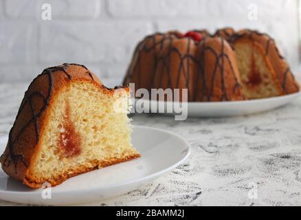 Kuchenscheiben auf einem Teller. Im Hintergrund steht der Kuchen selbst. Auf dunklem und hellem Hintergrund. Erdbeere und Creme mit Zucker füllen Stockfoto