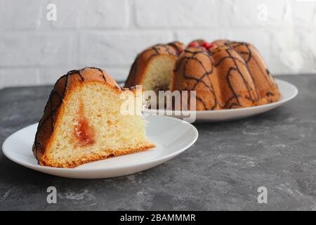 Kuchenscheiben auf einem Teller. Im Hintergrund steht der Kuchen selbst. Auf dunklem und hellem Hintergrund. Erdbeere und Creme mit Zucker füllen Stockfoto