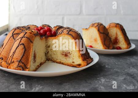 Kuchenscheiben auf einem Teller. Im Hintergrund steht der Kuchen selbst. Auf dunklem und hellem Hintergrund. Erdbeere und Creme mit Zucker füllen Stockfoto