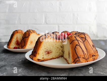 Kuchenscheiben auf einem Teller. Im Hintergrund steht der Kuchen selbst. Auf dunklem und hellem Hintergrund. Erdbeere und Creme mit Zucker füllen Stockfoto